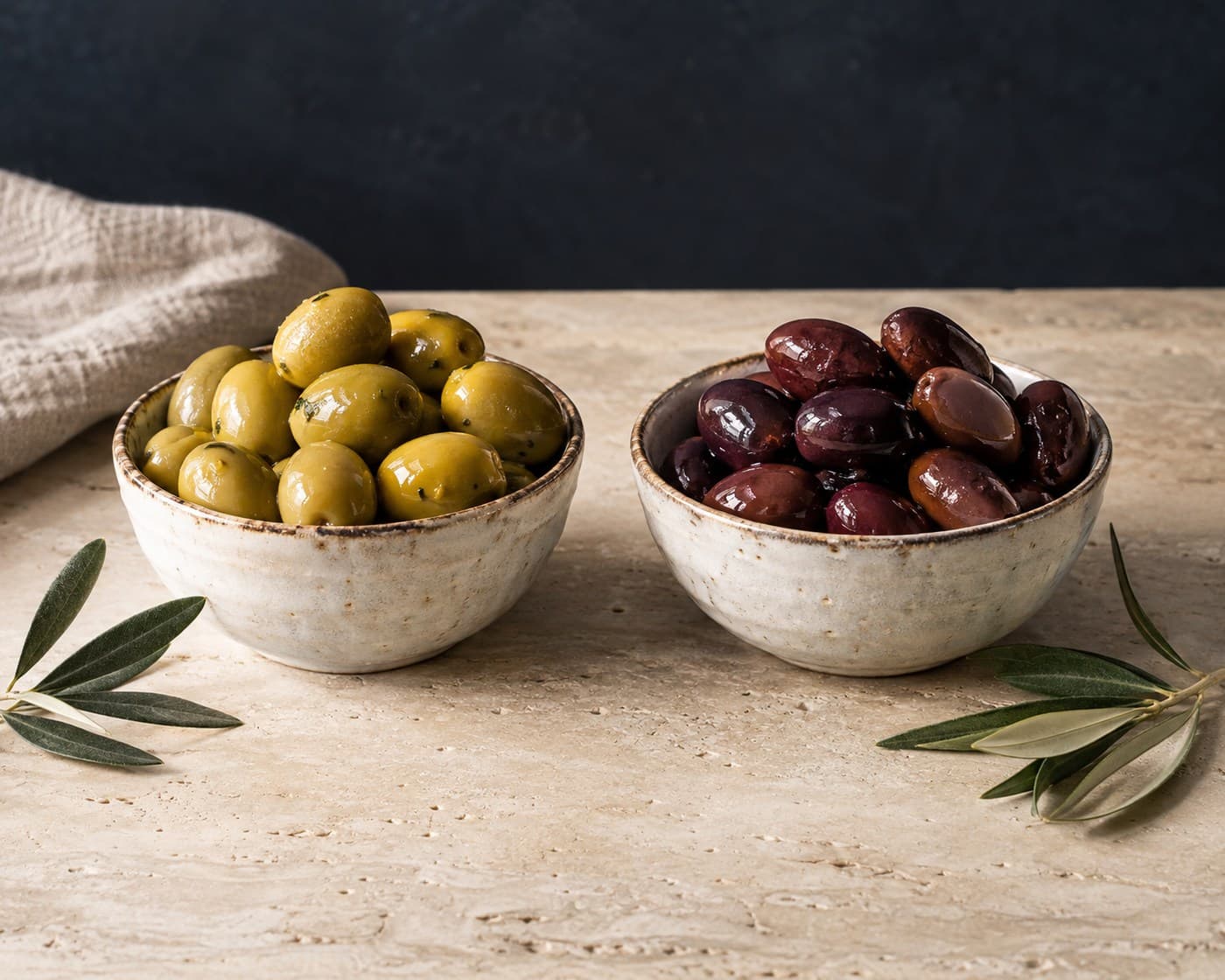 Green and dark table olives in separate ceramic bowls